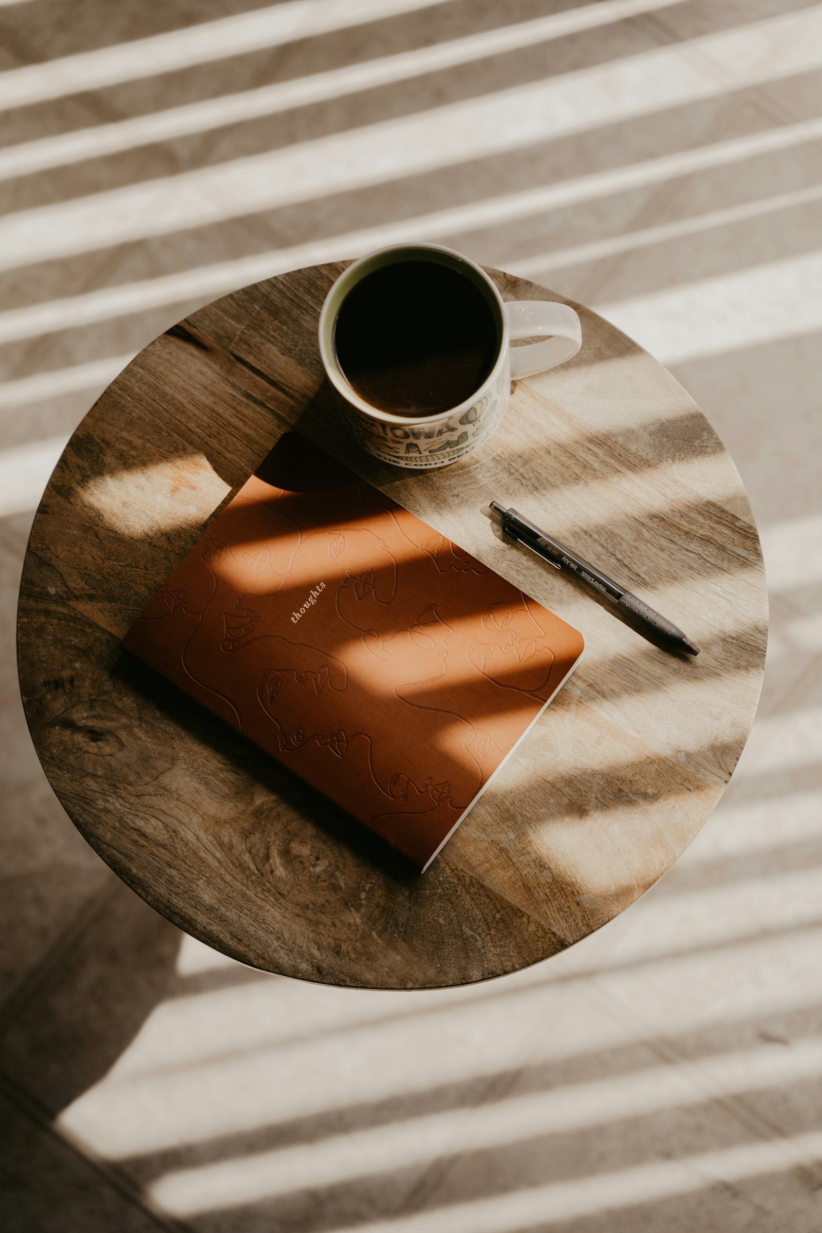 A notebook and pen on a wooden table, crossed by bands of sunlight