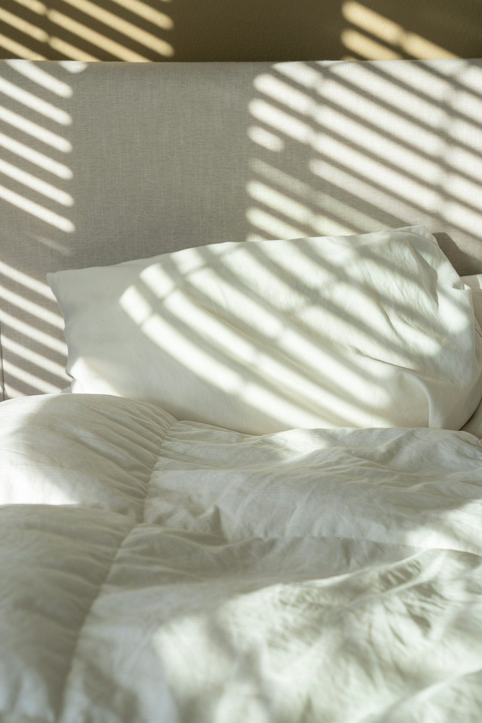 Soft white pillows striped with morning light through window blinds